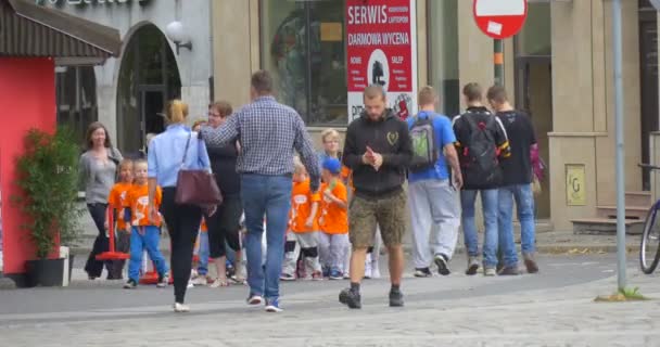 Groep van kinderen verschijnt van achter de hoek van de bouw van jonge geitjes in oranje T-Shirts lopen door de straat leidt de kinderen met hun leraar — Stockvideo