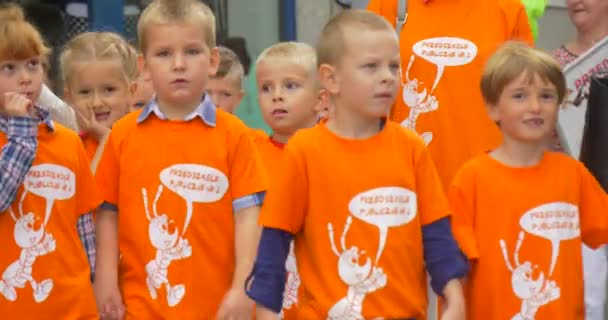 Des enfants en T-shirts orange marchent avec leur professeur dans la rue Dirigeant les enfants Les enfants sourient Parler tenant les bannières Le jour — Video