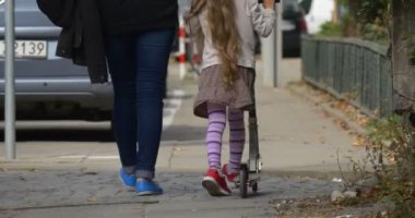 Anne küçük sarışın kız sokak ayakları kırmızı spor ayakkabılar mavi ayakkabılar yakın kadar kadın anne tarafından tekme Scooter sürme yürüyüş boyunca kız kızı uzak yürüme olmasıdır