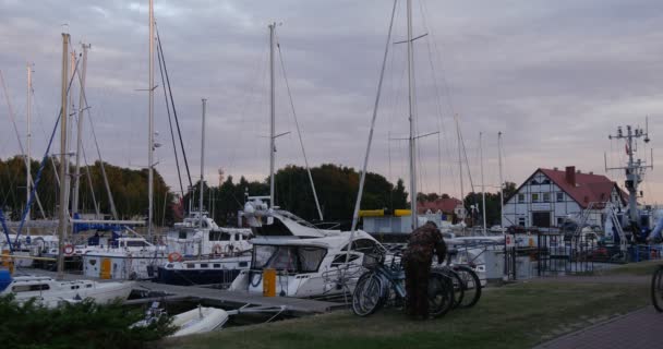 Man parkerar sin cykel kvinna rider på den cykel Man går till piren vita båtar läggs upp Yacht Club Port hamnen molnig sommardag solnedgång Leba Polen — Stockvideo