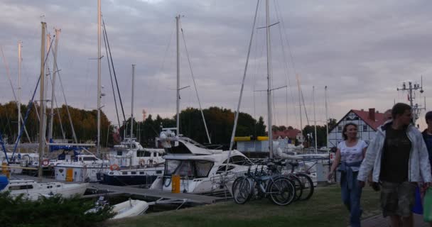 Groupe människor gå på trottoaren vita båtar läggs upp Yacht Club Port hamnen cykel parkering på Shore molnig sommardag solnedgång Leba Polen — Stockvideo