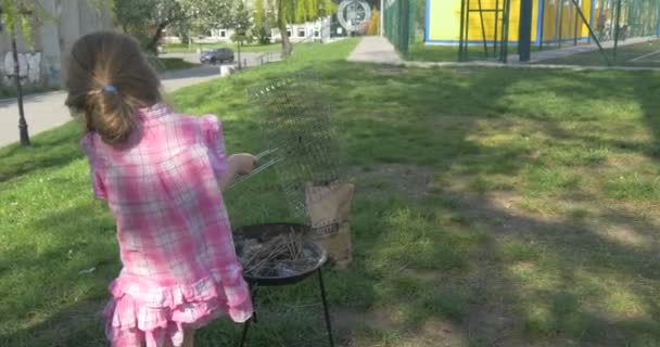 Bebé niña está preparando carnes a la parrilla en un vestido rosa sobre hierba verde — Vídeo de stock