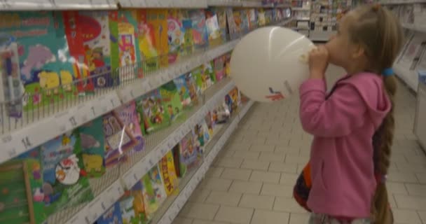 Baby-Mädchen im Supermarkt wählt Buch Ballon liest ein Buch und blättert die Seiten — Stockvideo