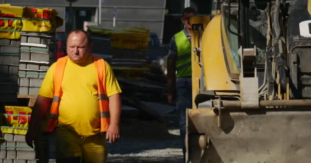 Sarı Ekskavatör duran iki işçi olan yürüyüş sarı iş giysisi paletleri ile blok kaldırım yol şehir sokak sokak yol tamir olduğunu — Stok video