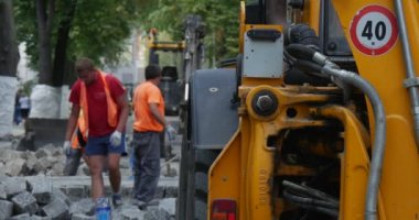 İşçilerin turuncu iş giysisi parke şehir sokak yol onarım sarı Ekskavatör yola yakındır ayakta bloklar Transpors yığın bloklar için