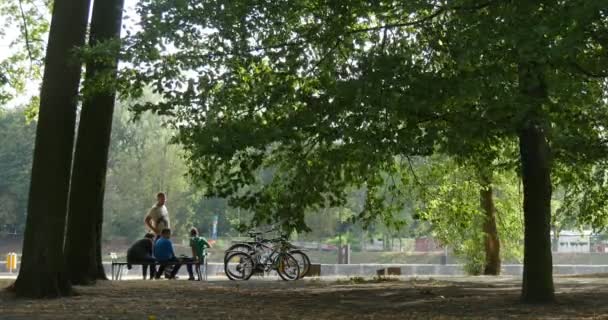Aile insanlar anne baba çocuk uzaktan oturuyor tezgah Park insanlar var, geri kalan Bisiklet insanlar Park orman spor yakın duruyorsun — Stok video