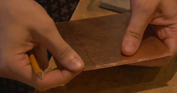 Les mains de l'homme prennent le morceau carré de plaque de cuivre Commencez à moudre les bords La main tient le crayon Préparez la plaque pour faire une image de gravure — Video
