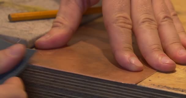 Las manos del hombre Tome la pieza cuadrada de la placa de cobre Comience a moler los bordes El lápiz está sobre la mesa Prepare la placa para hacer una imagen de grabado — Vídeo de stock