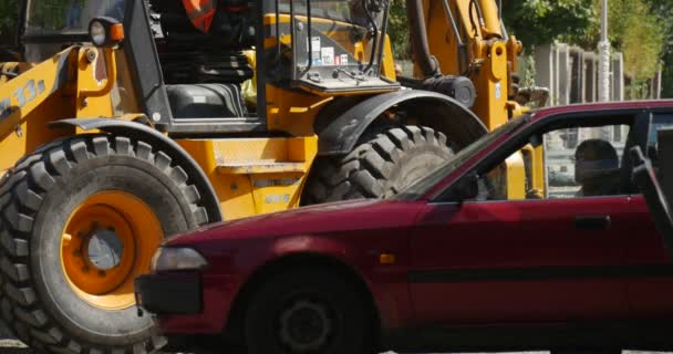 A máquina escavadora amarela está trabalhando com rodas de escavadeira de colher Close Up Red Car Silver Car estão passando por motoristas de carros ensolarados ao ar livre Road Repair — Vídeo de Stock