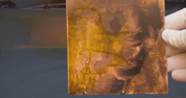 Les mains de l'homme dans des gants de protection faisant la gravure d'une plaque de cuivre dans l'acide dans un récipient L'homme a sorti les plaques gravées sur une plaque de cuivre 