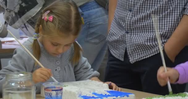 Lány közelről a festmény Brush gyerekek létrehozása kézzel készített termékek jótékonysági aukció férfi és nő az asztalnál — Stock videók