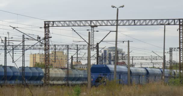 Twee goederentreinen staan op de spoorrails blauwe en grijze tanks blauwe goederen wagons ondersteunt van spoorweg contact netwerk gebouwen op de achtergrond — Stockvideo