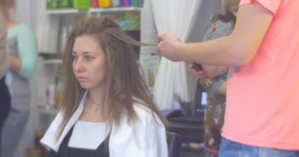 Stylist Parrucchiere in Rosa T-Shirt Making Hairstyle Smal Riccioli Capelli Volume di stiratura dei capelli Ferro da stiro per una donna con capelli lunghi Salone di bellezza — Video Stock