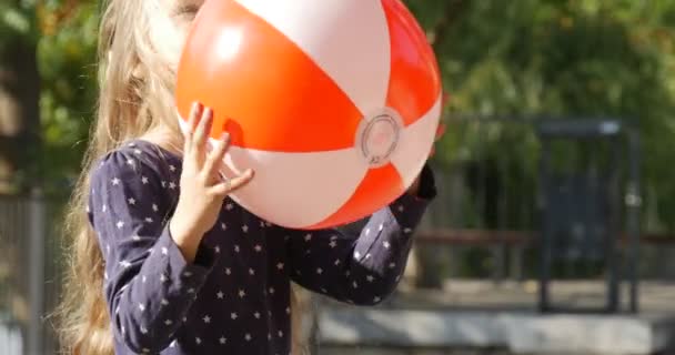 Klein meisje gezicht close-up met lange eerlijke haren speelt bal gooit de bal vangt de bal meisje is glimlachend wandelen park bomen hek zonnige dag — Stockvideo