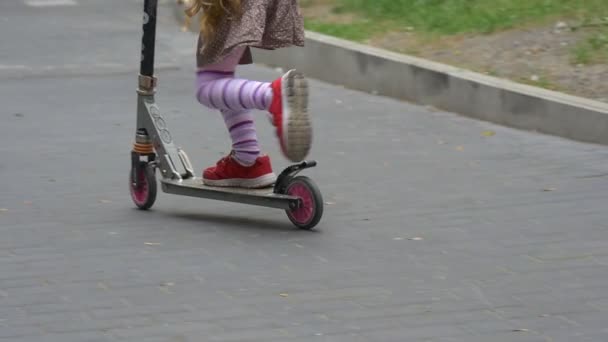 小金发女孩红色运动鞋特写倾斜女孩是骑踢滑板车向上由山西蒂街路标停车停车汽车慢动作 — 图库视频影像