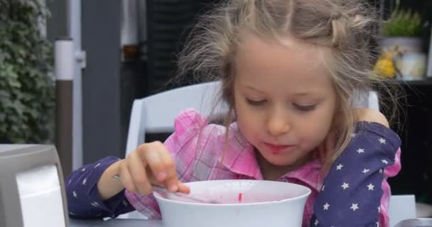 Маленькая блондинка сидит стул стол есть красный суп Borsch в кафе девушка не любит еду на открытом воздухе зеленый ползучий завод белый стул — стоковое видео