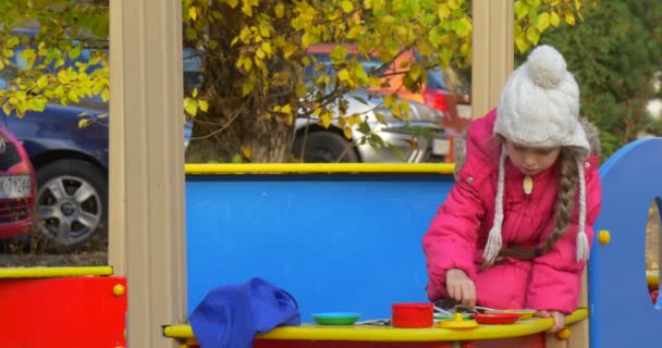 Liten blond flicka blandar sanden i Toy Plate spela leksak rätter leksak mat gafflar sked flicka spelar i sandlådan på Playground — Stockvideo