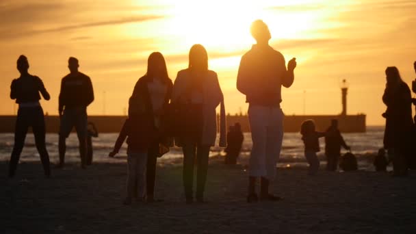 Ludzie latać kite sylwetki są patrząc w górę rodziny chodzą wzdłuż morza grając Frisbee Pier Yellow Sunset International kite Festival — Wideo stockowe