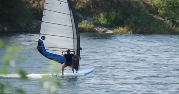 Man på vindsurfingbräda med segel flyter snabbt av vattnig yta man är i Windsurf kostym flod sand banker små vågor — Stockvideo