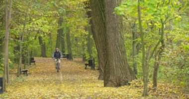 Ushanka şapka ile kürk kulak kapakları sıcak ceket adam sırt çantası ile erkekte sonbahar boş banklar sokakta Park tarafından fotoğraf makinesi doğru bisiklet sürme