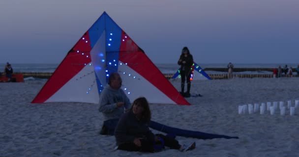 Bunte Drachen mit kleinen bunten Lampen auf dem Sand bereit, Menschen am Strand Nachtflüge leuchtender Drachen auf dem Drachenfest leba poland fliegen — Stockvideo