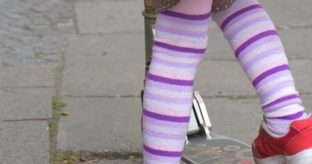 Flicka på en Kick Scooter flicka i kjol med blonda hårstrån står med Kick Scooter på gatan sätta hennes ben till Scooter Tilt upp flickans ansikte närbild — Stockvideo