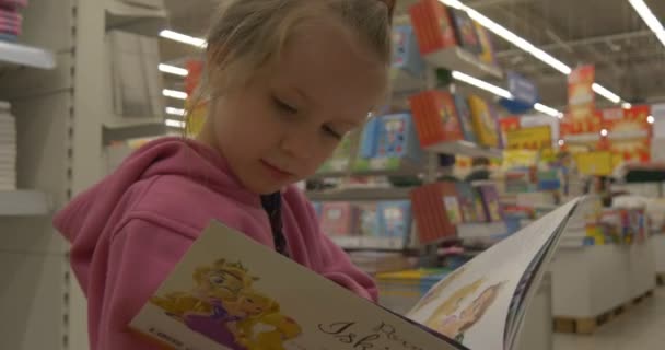 Baby-Mädchen im Supermarkt wählt Buch liest ein Buch und blättert um — Stockvideo