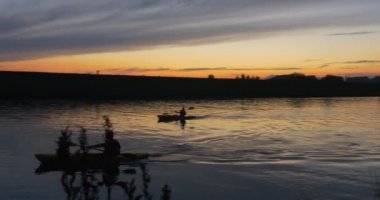 İki kişi adamlar kayaklar üzerinde su ağaçlarının Silhouettes yansıma parlak günbatımı pembe ve sarı gökyüzü dalgalanan kürekler nehir gölet ile kürek