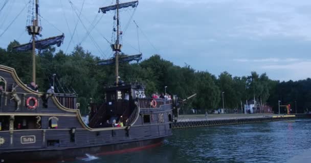 Black Sailboat With People On The Board Fast Swims Into The Harbor Back View People Walk On The Quay Calm Water Cloudy Sky Summer Evening Leba Poland — Stock Video