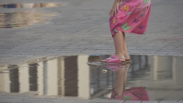 Den lilla flickan klädd i en sommar kläder spelar i pöl på trångt gata. — Stockvideo