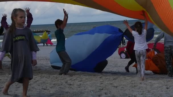 Kinder schieben beim internationalen Drachenfest in Leba, Polen, einen bunten Luftschwimmer in die Luft, damit dieser den Wind fängt. — Stockvideo