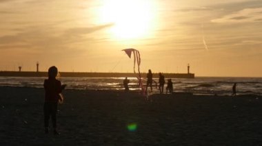 Küçük kız siluet sinekler Sandy Beach insanlar aileler siluetleri üzerinde küçük uçurtma sahil dalgalar yürüyüş günbatımı Uçurtma Şenliği sarı
