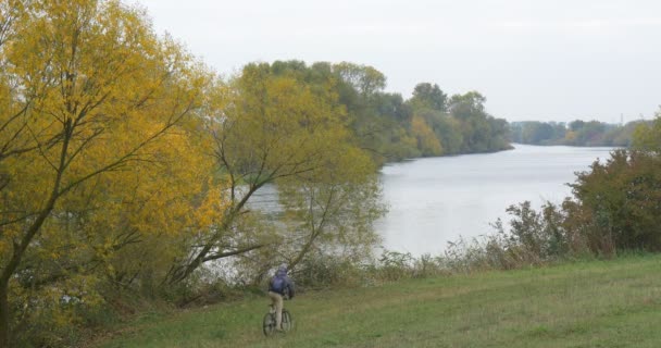 Hombre en sombrero de Ushanka con y chaqueta viene montar en bicicleta a la orilla del lago río bajó de la bicicleta dejó la bicicleta y caminar hacia el agua — Vídeos de Stock