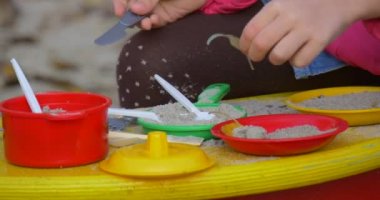 Küçük kız o plastik bıçak Görünümü Kapat güneşli bir sonbahar gün ile renkli oyuncak yemekleri kızın elleri ile çalış sarı oyuncak mutfak masasında oturuyor