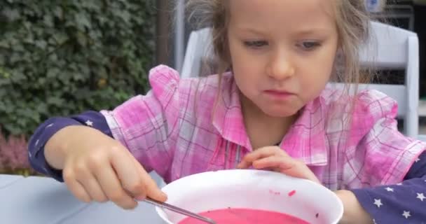Девушка в розовой рубашке садится за стол и ест, потом толкает тарелку и кладет подбородок на стол. — стоковое видео