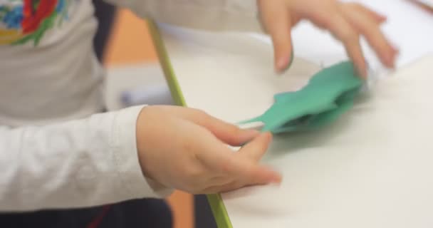 Niña está sentada o de pie en la mesa haciendo un juguete de papel de verde pedazo de papel manos de cerca jugando en el aula de la biblioteca central — Vídeos de Stock