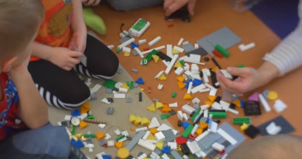 Crianças pequenas com seu professor estão sentados em pés de chão Pernas mãos de perto e jogando um construtor de brinquedos de plástico na Oficina Biblioteca Central em Opole — Vídeo de Stock