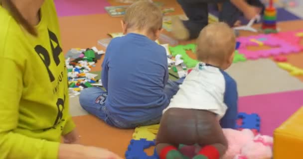 Małe dzieci z ich nauczyciel siedzą na podłodze i gry plastikowe zabawki chłopca Konstruktor jest indeksowania w centralnej biblioteki warsztaty w Polsce opolskie — Wideo stockowe