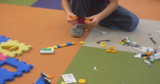 Liten unge pojke sitter på golvet och spelar plast leksak konstruktören och kastar ut en leksaksbil på centrala bibliotek verkstad i Opole Polen — Stockvideo