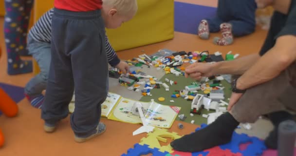 Małe dzieci z ich męskiego nauczyciela siedzą na podłodze i bawią się plastikowym konstruktorem zabawek w centralnej bibliotece warsztaty w Opolu Polska — Wideo stockowe