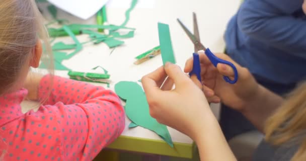 子供たちは、紙のおもちゃの先生の女性がおもちゃ作成の中央図書館ワークショップをクローズアップ緑の紙の手をカットするカラフルな紙で作業しています — ストック動画