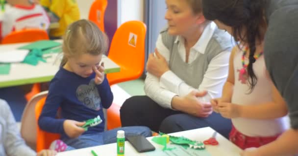 Kinder arbeiten mit buntem Papier machen ein Papier Krokodil mittleren Alters Lehrerin hilft dem Mädchen zentrale Bibliothek Werkstatt von Spielzeug erstellen — Stockvideo