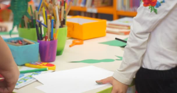 La ragazza è in piedi e gioca con la carta colorata che fa un insegnante di giocattoli di carta aiuta la ragazza a tagliare il laboratorio di giocattoli della biblioteca centrale di carta — Video Stock