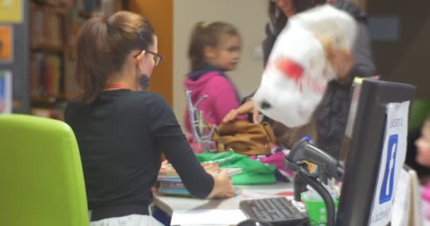 Mujer gerente está vendiendo dando libros y revistas a una mujer con niños aula de las hijas en el taller de la biblioteca central para la creación de juguetes — Vídeo de stock