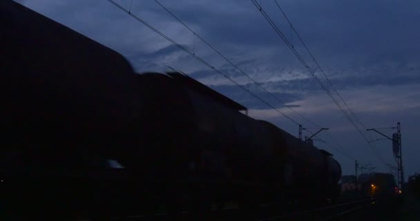 Šerá silueta nákladního vlaku železnice kontakt síť siluety stromů a staveb světla nočního města oblačno nebe podzim