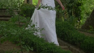 Beyaz düğün elbise gelin kadında yürüyüş yavaş yavaş aşağı Park gelin, Holding Her elbise Hayır yüz Parade, gelinler yaz yeşil ağaçların içinde olduğunu