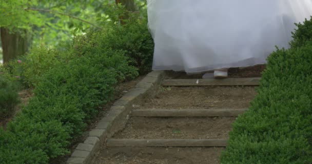 Kurzhaarige blonde lächelnde Frau in weißem Hochzeitskleid ohne Schultern flauschiges Kleid glückliche Braut geht unten im sattgrünen Parkkleid — Stockvideo