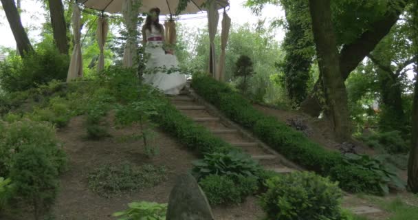 Donna sposa in abito guaina bianca con cintura rossa sposa con i capelli sciolti a piedi al piano di sotto lentamente da sotto la tenda su una cima di Hill Brides Parade — Video Stock