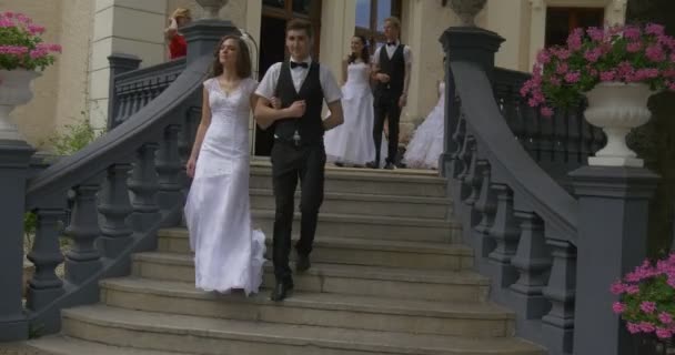 Ζευγάρι νύφη με τα μαλλιά που είναι χαλαρά και γαμπρός είναι περπάτημα κάτω νύφη προσεγγίσεις σε γυναίκες θεατές στα λευκά φορέματα άνδρες στα κοστούμια νύφες παρέλαση — Αρχείο Βίντεο