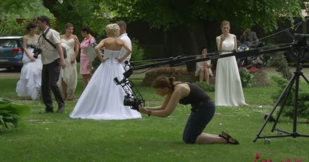 Pessoas Mulheres de vestido branco Noiva e homens Camera Crew As pessoas estão olhando para Tablet Screen Woman está configurando a câmera em um Stand Brides Parade — Vídeo de Stock